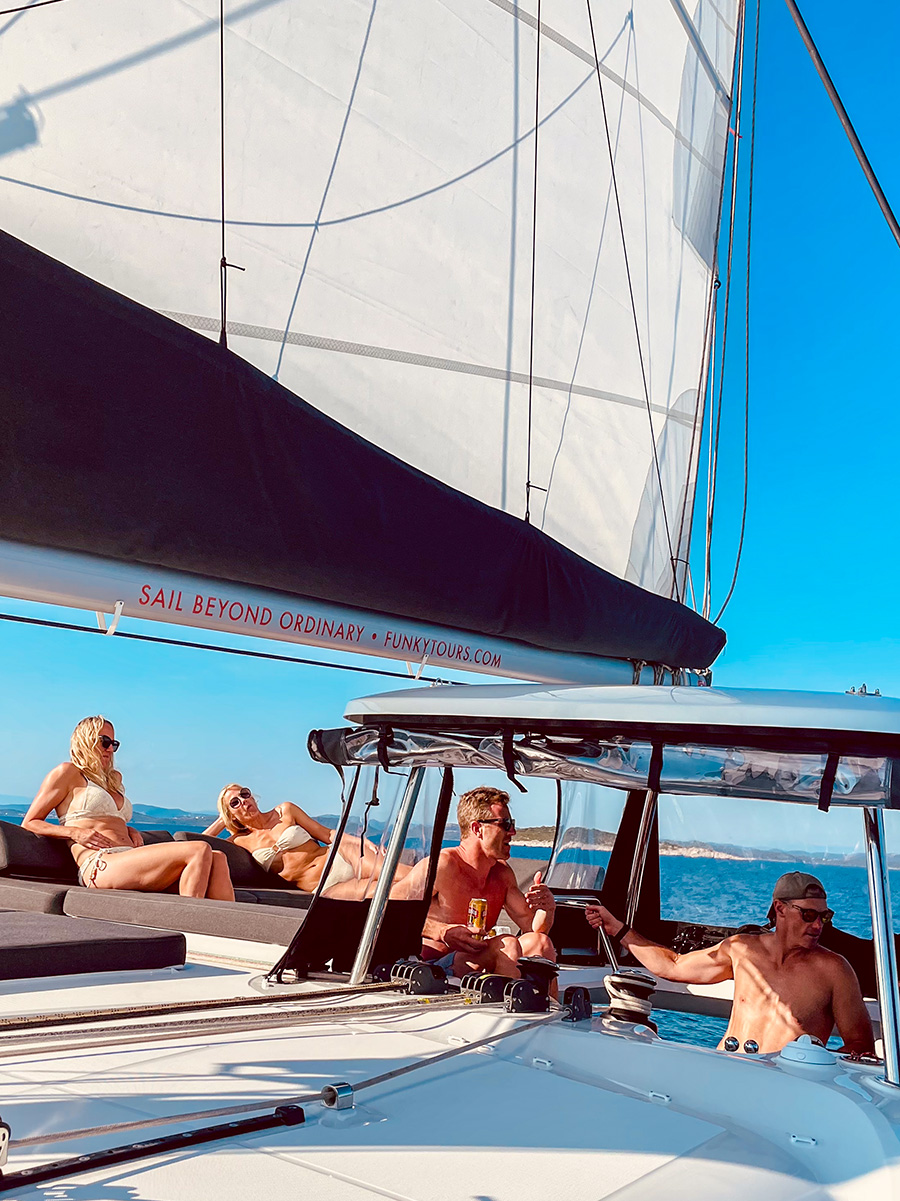 Guests relaxing on the forward deck beneath the catamaran sails